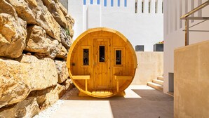 A wooden sauna with a circular door, set against a white wall and a rocky background. - Villa Yara | Pool - BBQ - Bar (Mijas)
