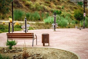 A park with exercise equipment, a bench, and a trash bin.