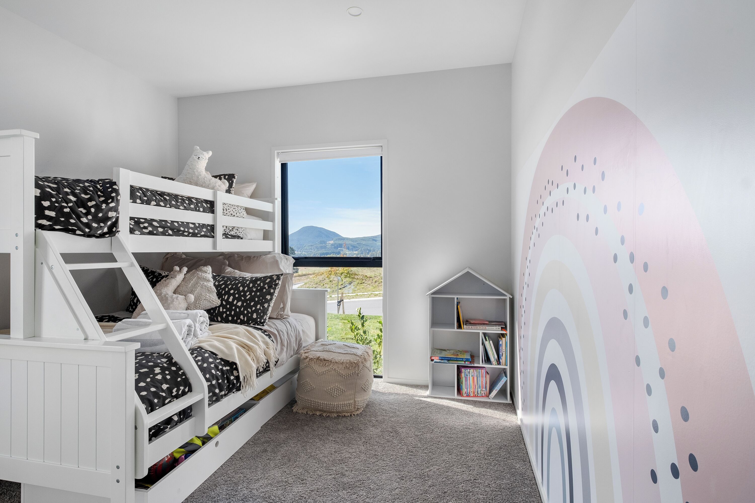 A child’s bedroom with bunk beds, a bookshelf, and a large window with a view.