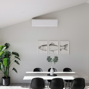 Un espace repas moderne avec une table blanche, des chaises noires, une plante en pot et trois illustrations de poissons encadrées accrochées au mur.