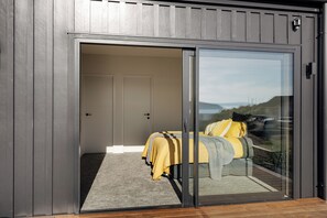 Une chambre moderne dotée d’une porte-fenêtre coulissante donnant sur un balcon, d’un lit recouvert d’une couverture jaune et offrant une vue sur l’extérieur.