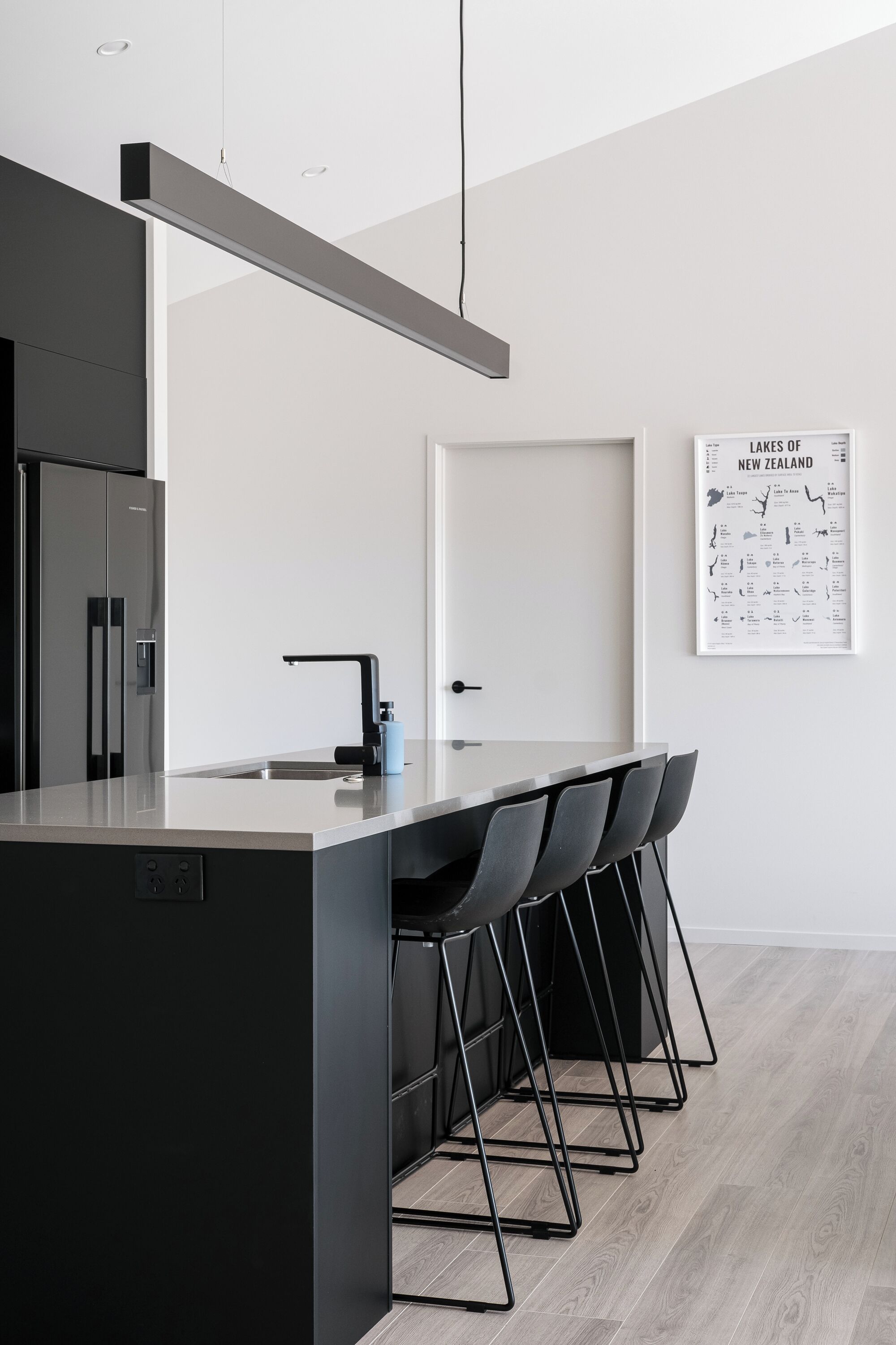 Una cocina moderna con una isla central, sillas negras y un mapa enmarcado en la pared.