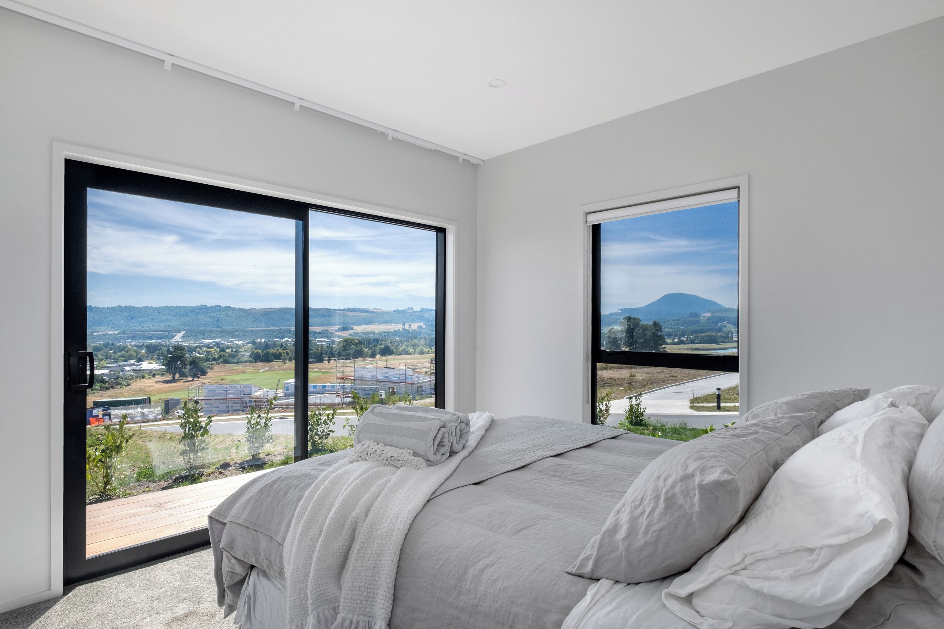 A bedroom with a large bed, two windows, and a view of a landscape.