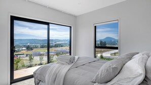 Ein Schlafzimmer mit einem großen Bett, zwei Fenstern und Blick auf eine Landschaft.