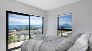 A bedroom with a large bed, two windows, and a view of a landscape.