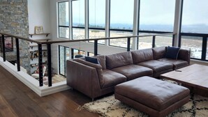 Ein geräumiges Wohnzimmer mit einer großen Eckcouch, einem Holztisch und Blick ins Freie durch große Fenster.