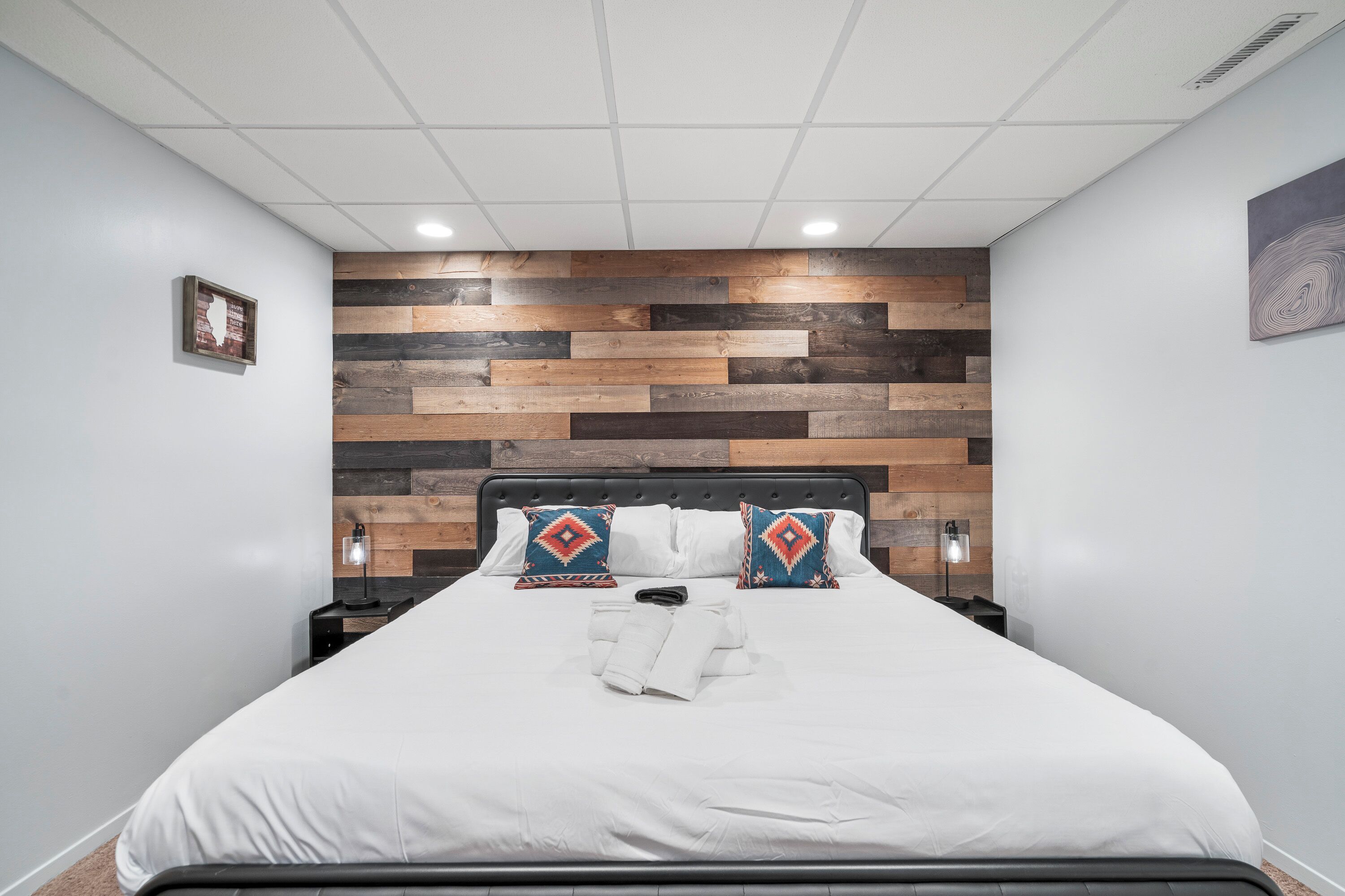Ein modernes Schlafzimmer mit einer Holzwand, einem schwarzen Kopfteil, weißer Bettwäsche und zwei Nachttischlampen.