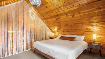 A bedroom with a wooden ceiling, a bed with white bedding, a nightstand with a lamp, and a decorative hanging light fixture.