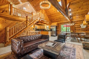 L’intérieur de cette vaste cabane en rondins est agrémenté d’un canapé en cuir, d’une table basse en bois et d’un coin repas avec une grande table et des chaises.