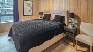 Un dormitorio con una cama grande, dos mesitas de noche con lámparas, una silla y una ventana con vista a un edificio.