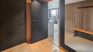Una habitación con piso de madera, una puerta oscura y vistas a otra habitación con ventana y un banco.