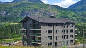 Un edificio moderno de varios pisos con balcones, frente a un paisaje montañoso.