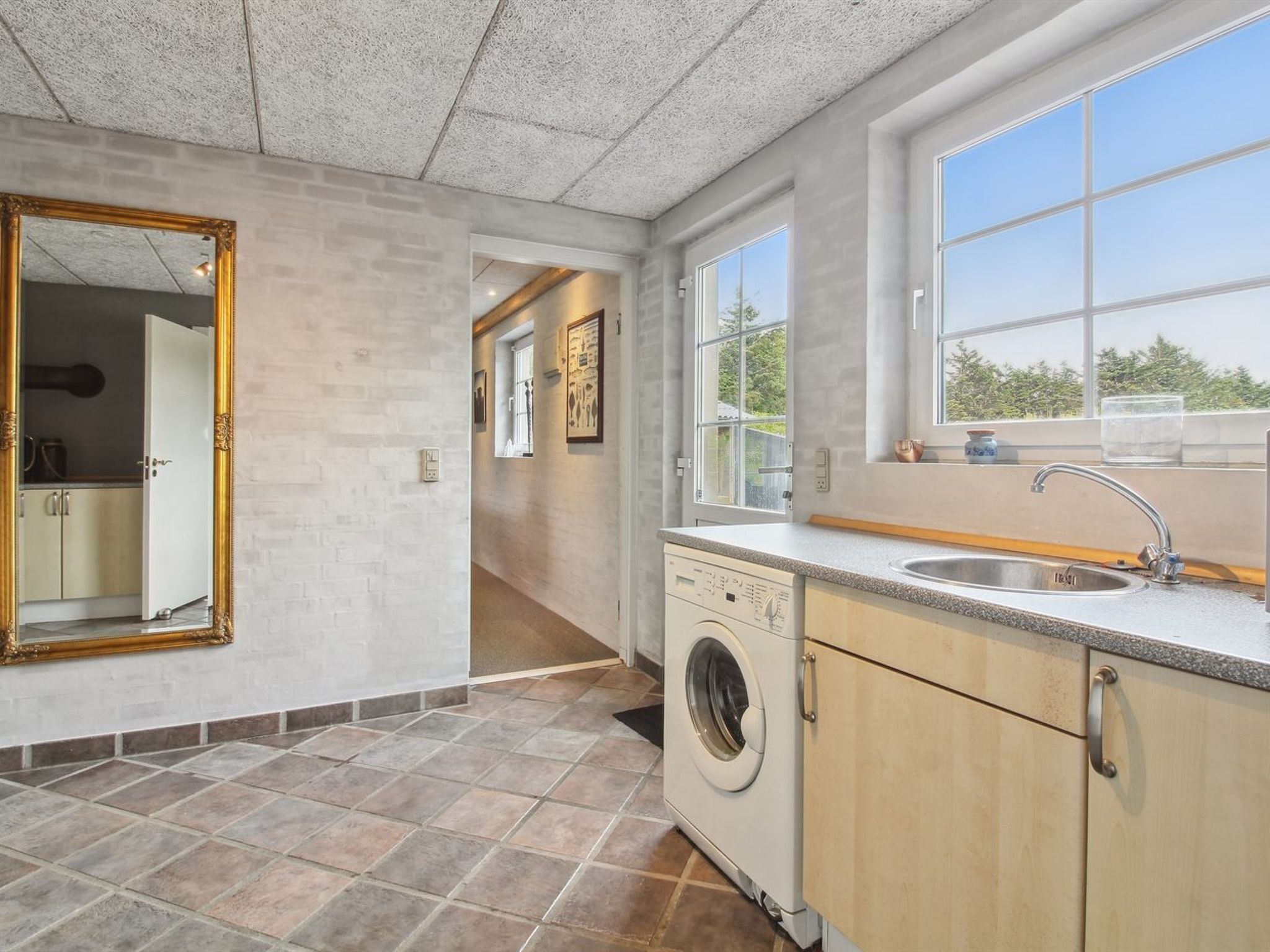 A laundry room with a washing machine, a sink, and a large mirror.