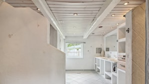Ein Flur mit weißen Wänden und Fliesenboden, der zu einem Badezimmer mit Waschbecken und Spiegel führt.