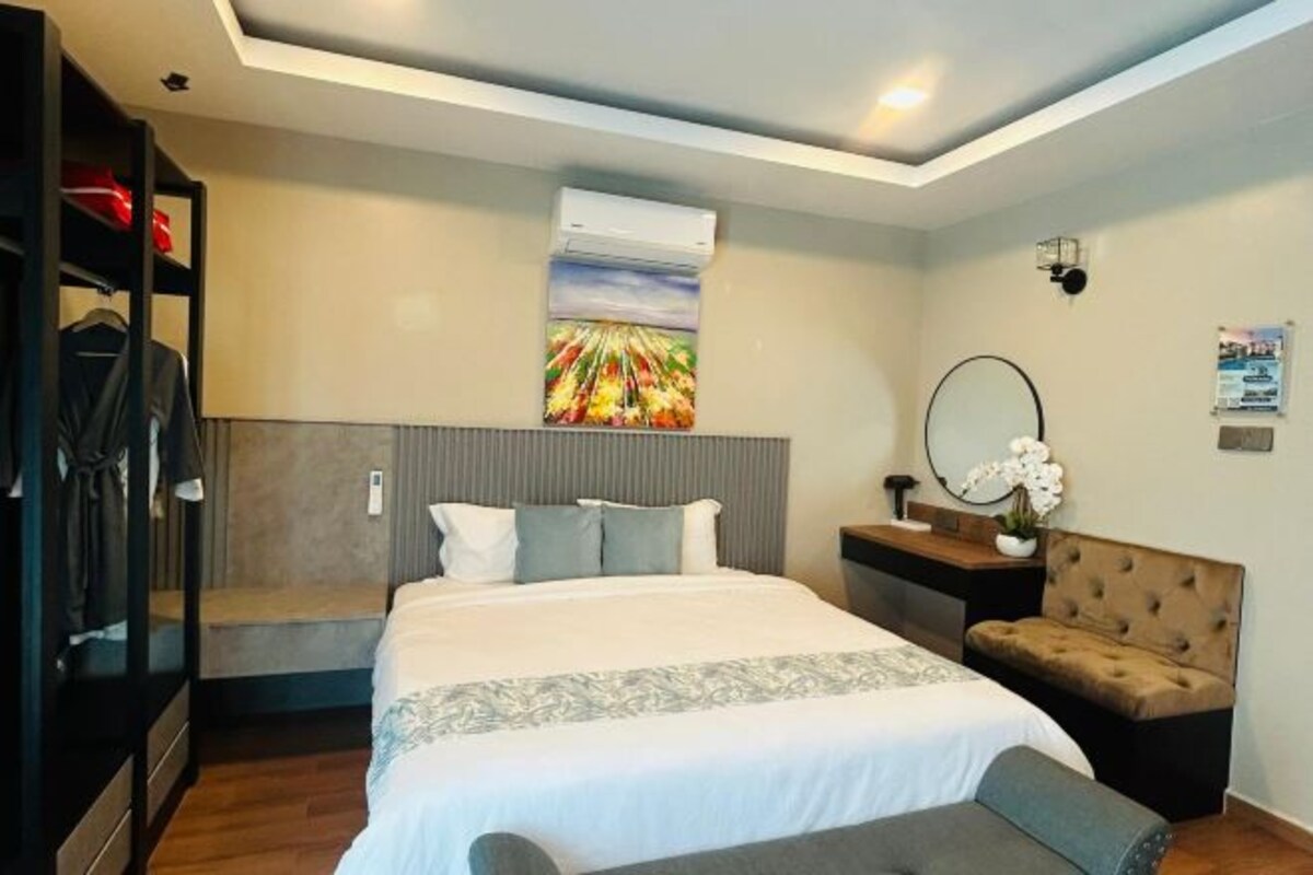 Une chambre d’hôtel comprenant un lit, une banquette, une armoire, une table de chevet avec un miroir et un climatiseur fixé au mur.