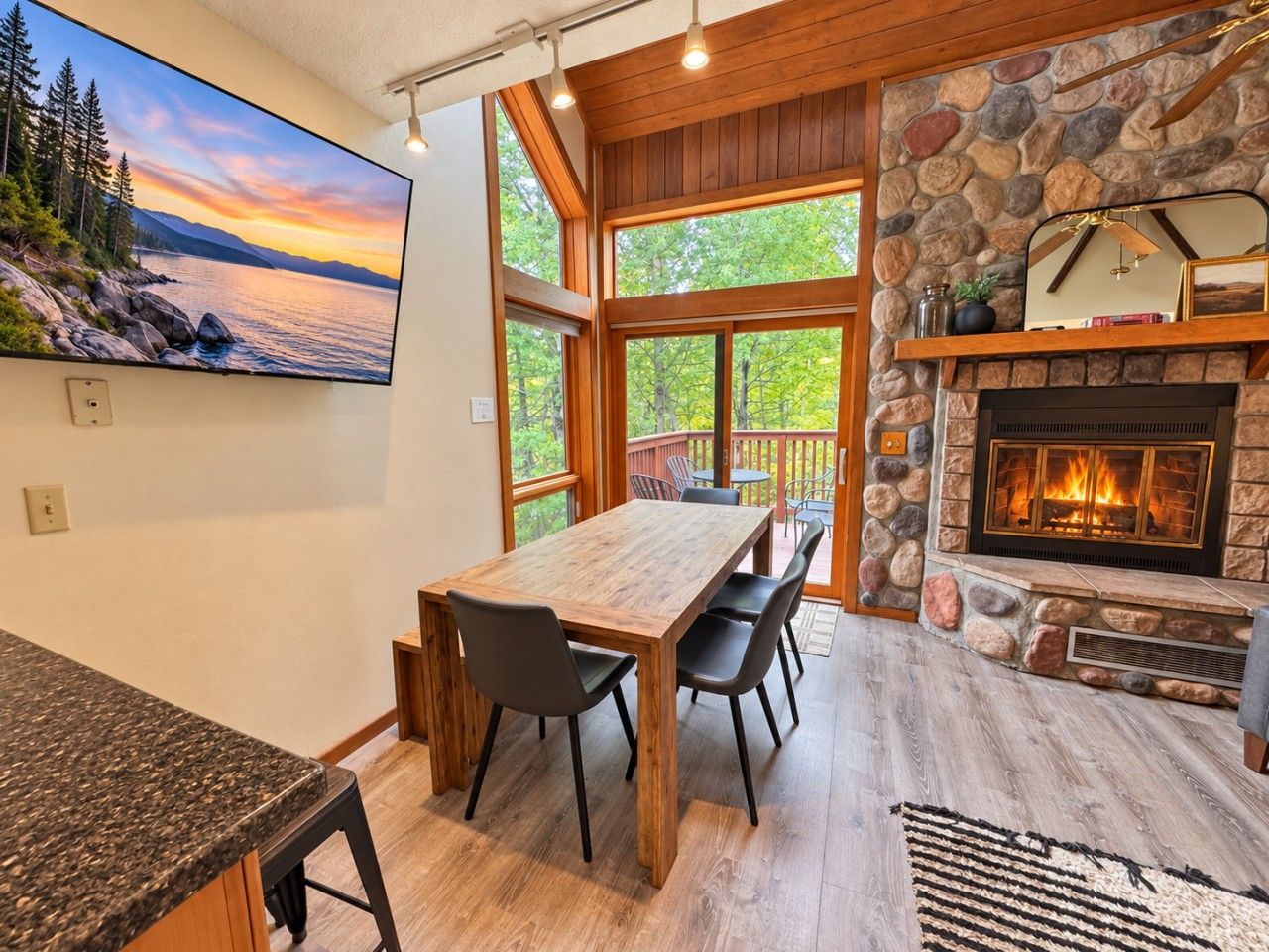 A modern kitchen with a large island, a stone fireplace, and a dining area with a view of the outdoors.