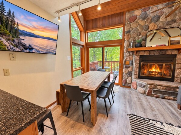 A modern kitchen with a large island, a stone fireplace, and a dining area with a view of the outdoors.