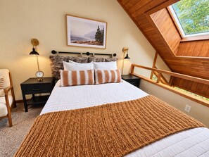 Une chambre à coucher avec un grand lit, une tête de lit en bois, un puits de lumière et un tableau encadré au mur.