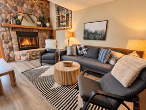 Un salon chaleureux avec une cheminée en pierre, un canapé, des fauteuils et une table basse.
