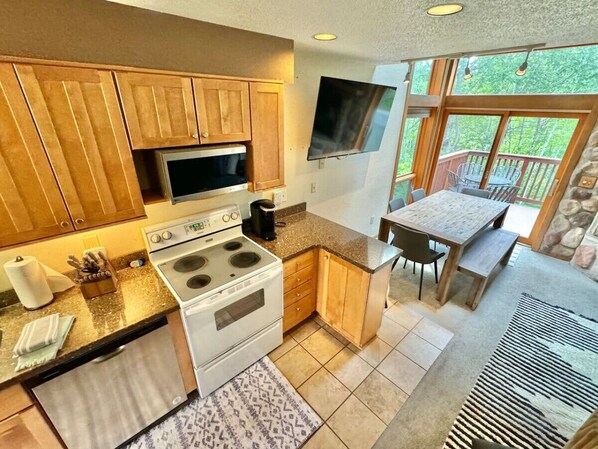 A kitchen with wooden cabinets, a stove, a microwave, and a dining area with a table and chairs. - 3-bed Family Friendly | Ski-In/Out| Pool & Hot Tub (Lutsen)