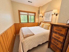 Une chambre à coucher avec un lit, une commode en bois, une fenêtre et une lampe fixée au mur.