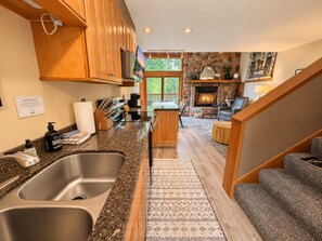 A kitchen with granite countertops, wooden cabinets, a built-in dishwasher, and a stone fireplace.