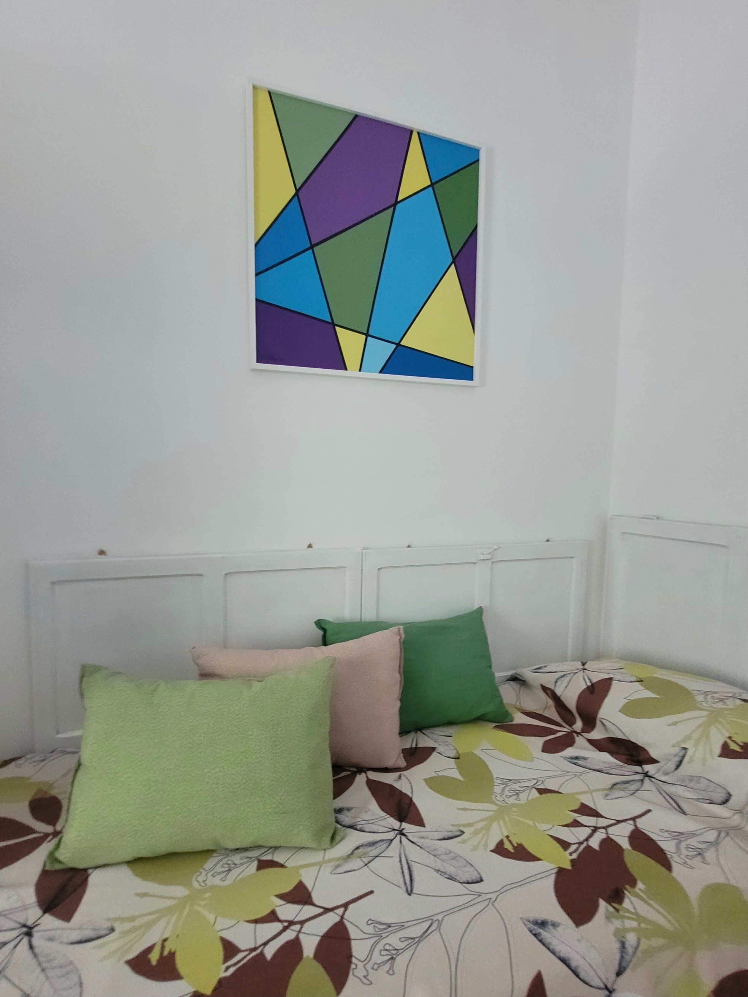 A bed with a floral-patterned bedspread, a geometric artwork on the wall, and two pillows.