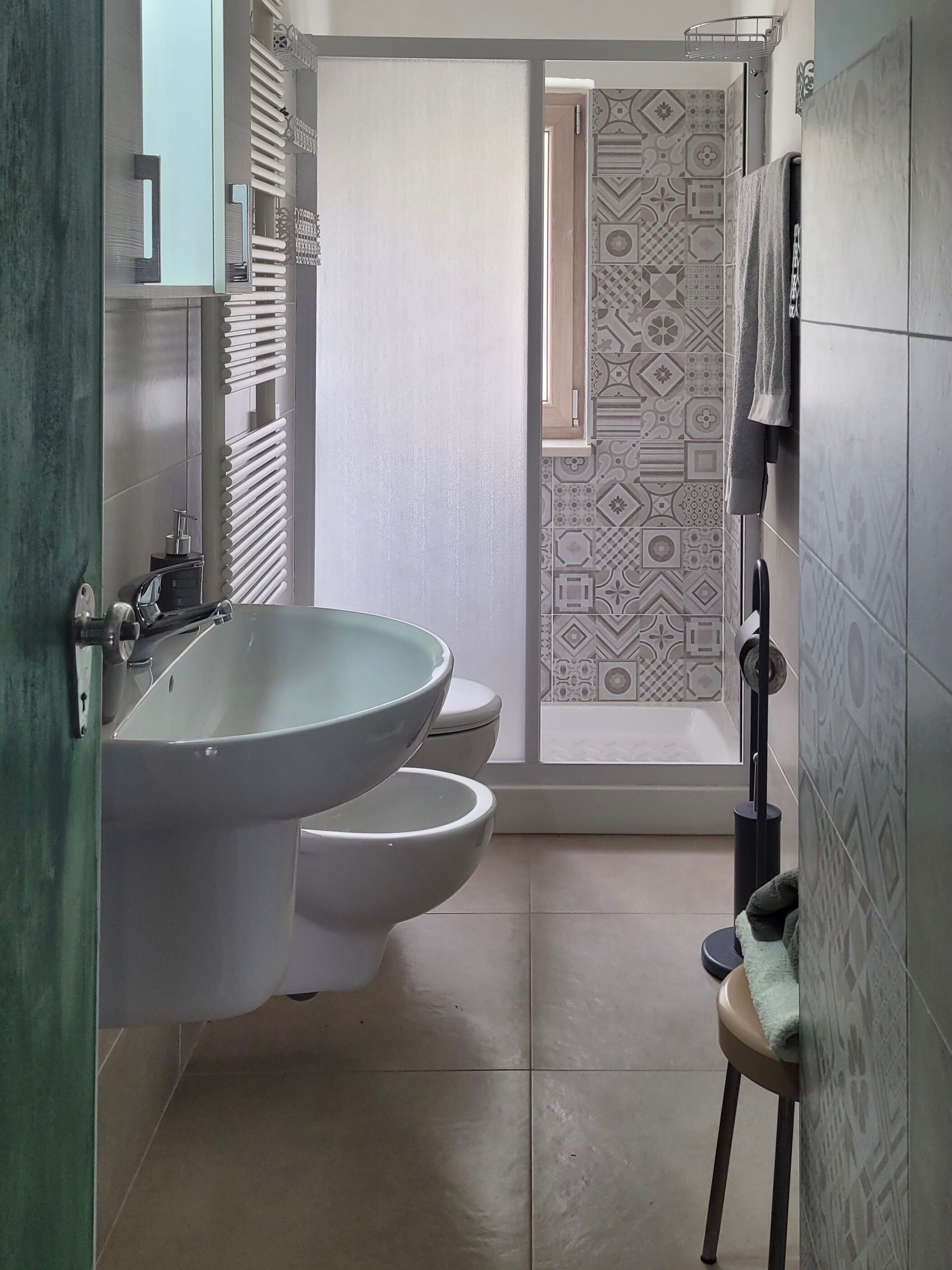A bathroom with a large sink, two toilets, patterned tiles, and a towel rack.