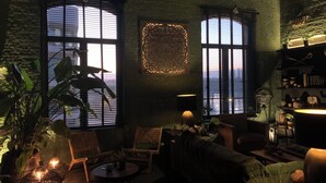 A cozy living room with a view of the sunset through large windows, wicker furniture, and a bookshelf.