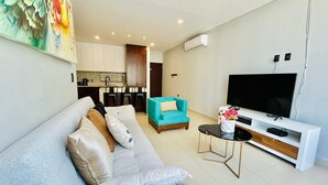 A modern living room with a sofa, a teal armchair, a coffee table, and a TV. - Cipres Apartments (Mazatlán)
