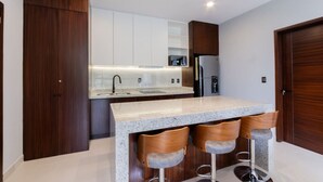 A modern kitchen with a granite countertop, stainless steel appliances, and wooden cabinetry. - Cipres Apartments (Mazatlán)