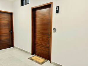 A hallway with two wooden doors, a doormat with the word "Welcome", and a number sign indicating room 3.
