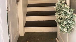 Eine enge Treppe mit weißen Wänden und schwarzen Stufen, die zu einer Tür oben führt.