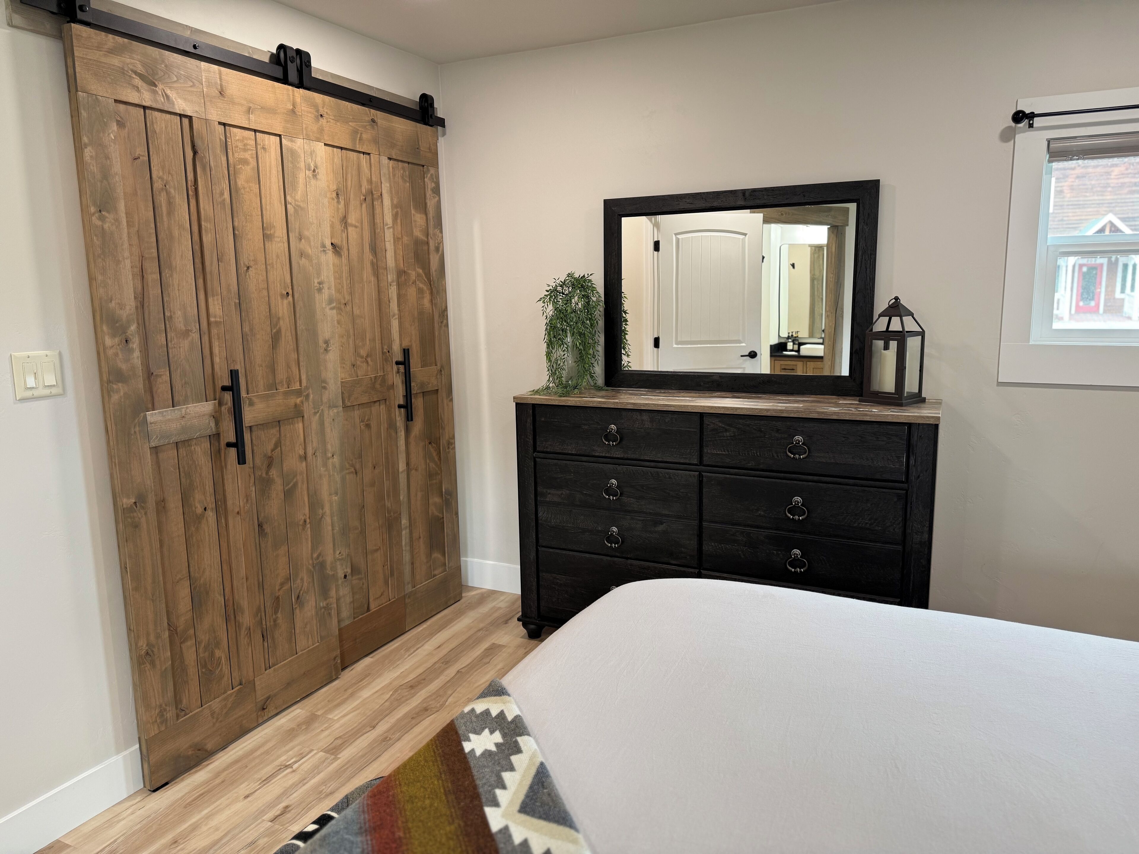A bedroom with a wooden sliding door, a dresser with multiple drawers, a large mirror, and a bed with a patterned rug.