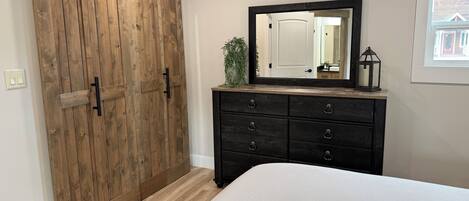 A bedroom with a wooden sliding door, a dresser with multiple drawers, a large mirror, and a bed with a patterned rug.