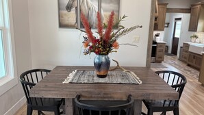 A dining table with a vase of flowers, surrounded by chairs, in a room with wooden flooring and a kitchen in the background. - House in the heart of Darby, Montana
Fully remodeled. (Darby)