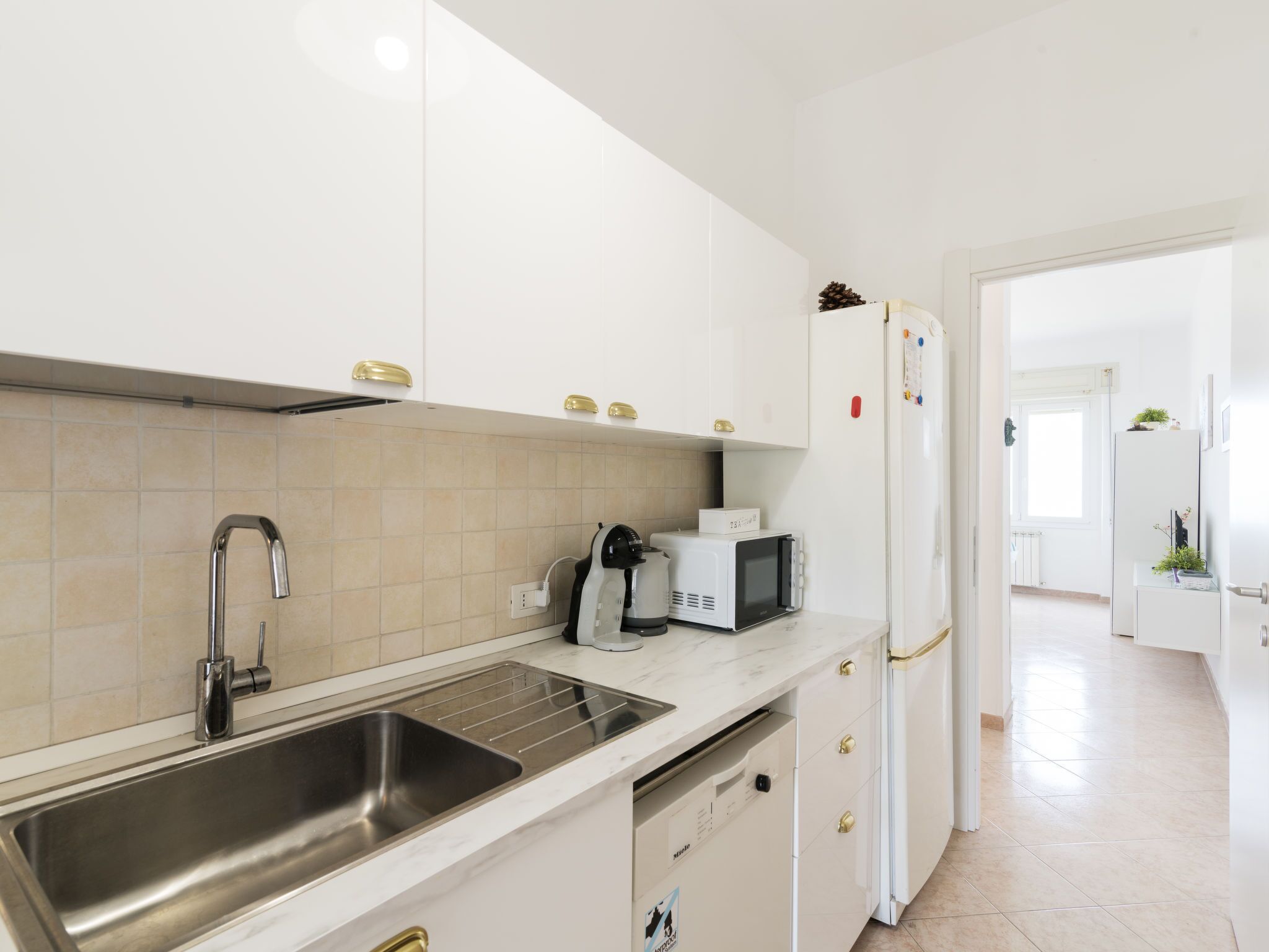 Una cucina moderna con mobili bianchi, un lavello in acciaio inossidabile, un forno a microonde e un frigorifero.