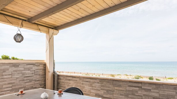 Een overdekt terras met een tafel gedekt voor twee personen, met uitzicht op een strand.