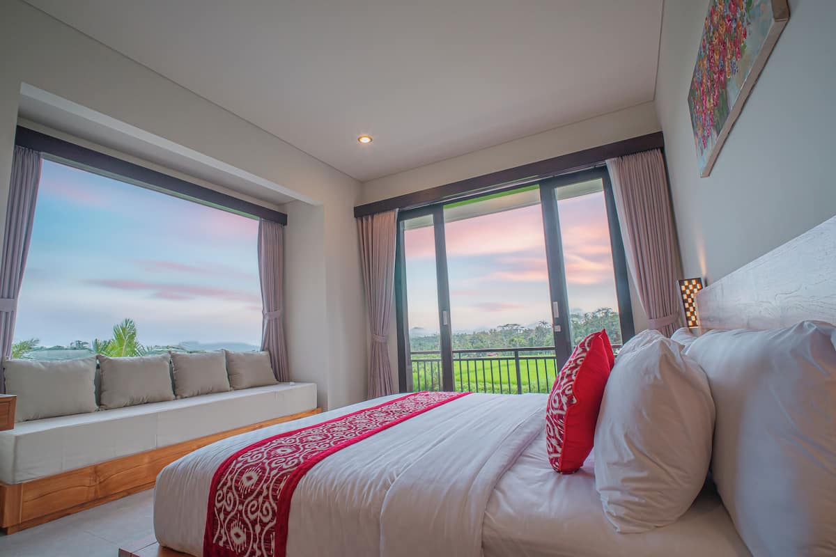 A bedroom with a large bed, a window seat, and a balcony with a view.