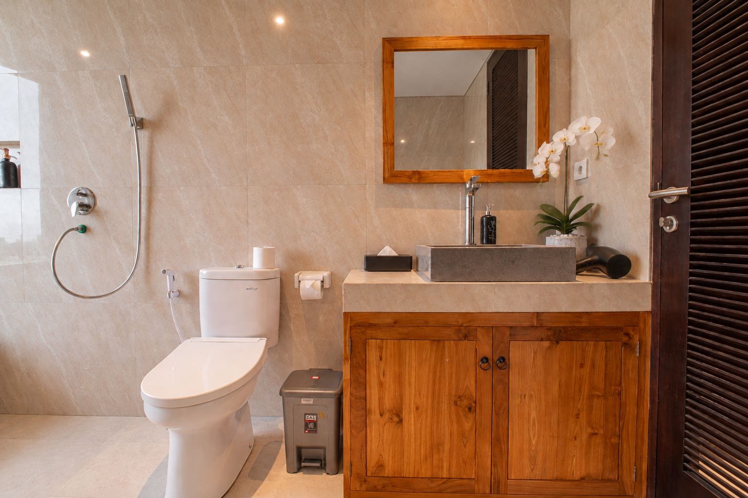 A modern bathroom with a toilet, a shower, a sink with a mirror, and a wooden cabinet.