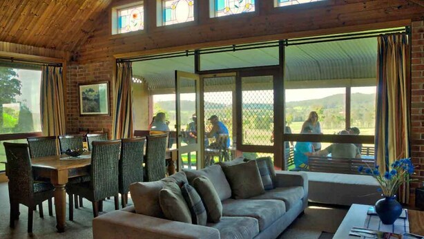 A cozy room with a wooden ceiling, a sofa, a dining table with chairs, and large windows with curtains. - Bluebush Estate - The Chalet - Stunning Country Views - Sleeps 10 (Rothbury)
