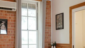 A bedroom with a brick wall, a large window with curtains, a wooden dresser, and a framed picture on the wall. - Bluebush Estate - The Chalet - Stunning Country Views - Sleeps 10 (Rothbury)