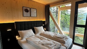 Ein Schlafzimmer mit einem großen Bett, Holzboden und einem Fenster mit Blick auf Bäume.