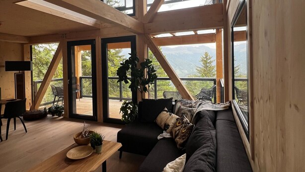 Ein modernes Interieur mit einer großen schwarzen Couch, einem Holztisch und Blick auf Berge durch große Fenster.
