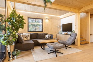 A cozy living room with a wooden ceiling, a sofa, a coffee table, a chair, and a TV. - Superior Chalet # 14 with Sauna & Hot Tub (Turrach)