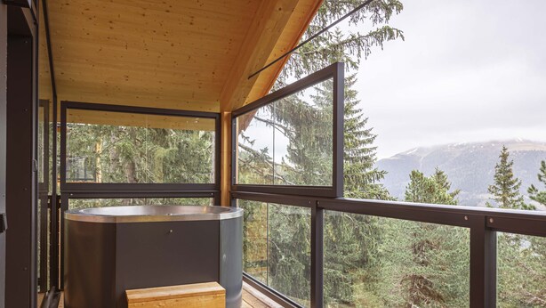 Una terraza moderna de madera con un jacuzzi y escalones de madera, con vista a una zona montañosa boscosa.