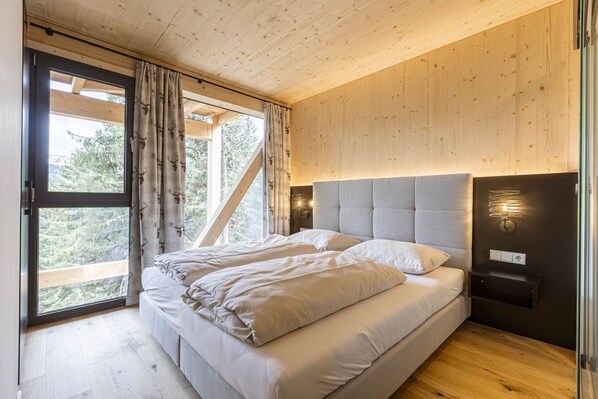 A bedroom with a bed, wooden ceiling, and a window with curtains. - Superior Chalet # 16 with Sauna & Hot Tub (Turrach)