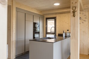 A modern kitchen with wooden walls, a central island, and built-in appliances. - Superior Chalet # 16 with Sauna & Hot Tub (Turrach)