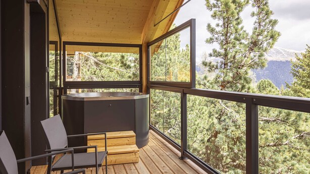 Eine Holzterrasse mit Whirlpool, Stühlen und Blick auf Bäume und Berge.