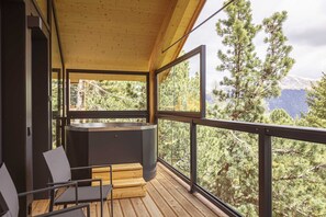 Eine Holzterrasse mit Whirlpool, Stühlen und Blick auf Bäume und Berge.